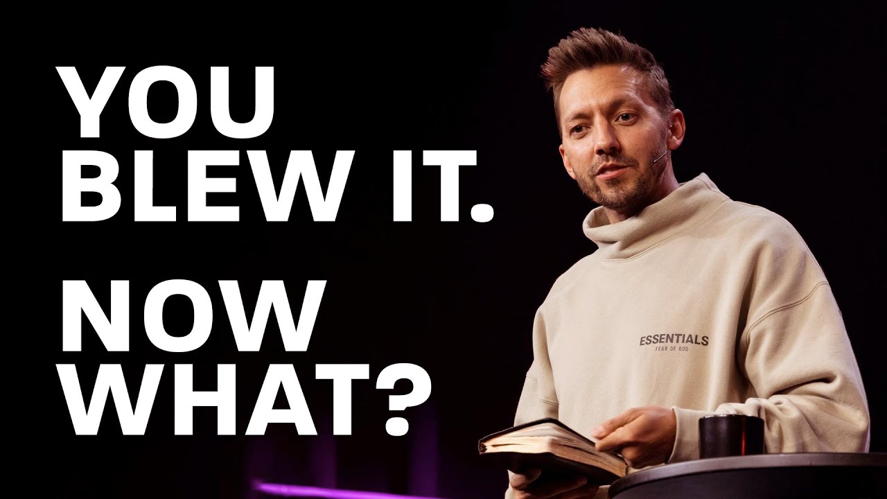 Pastor Levi Lusko standing with his left arm resting on a table and his right hand holding an open bible.